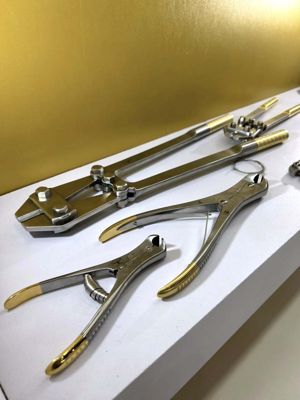 Alicates e cortadores de instrumental ortopédico com cabos dourados, expostos diante da parede dourada da FATO.