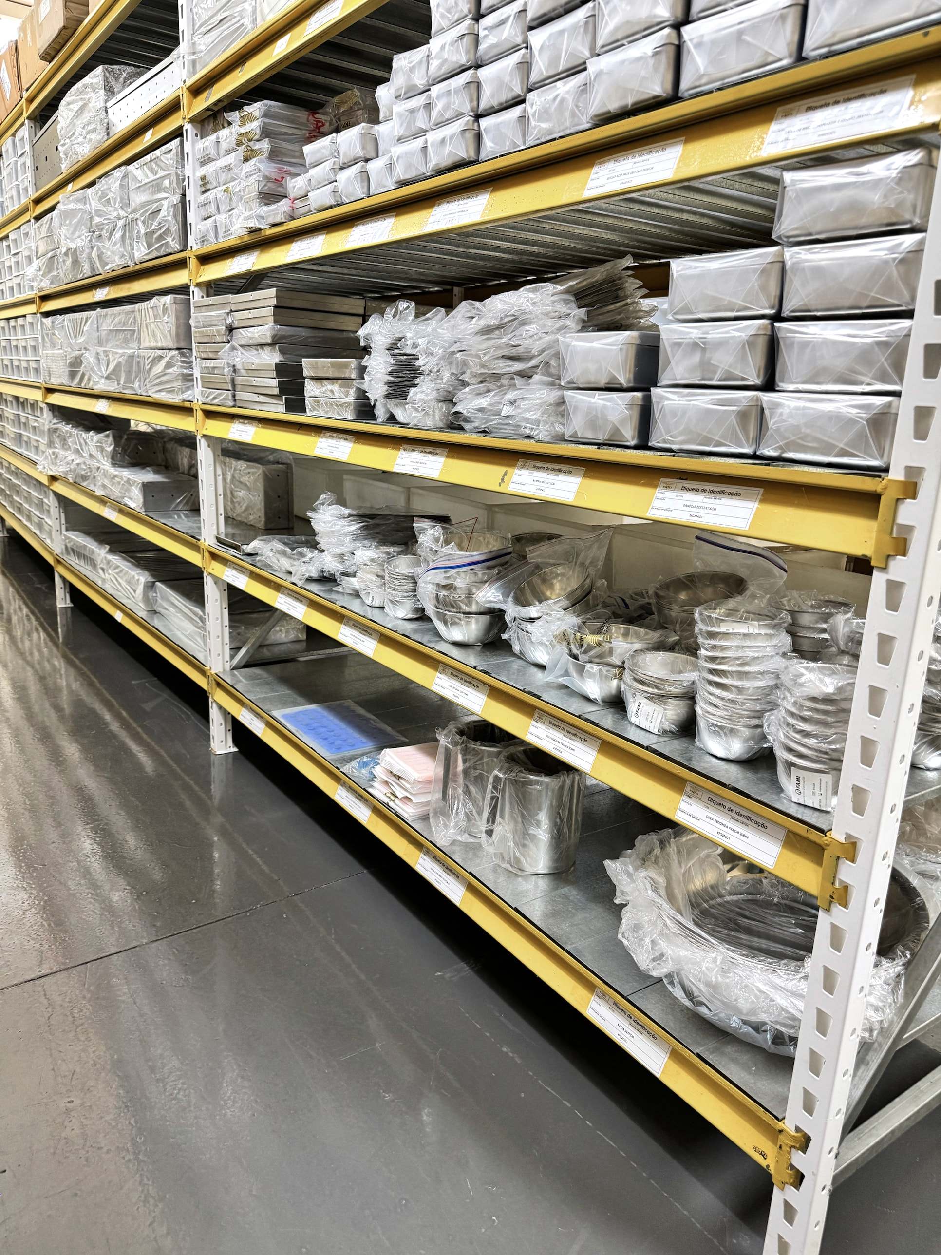 Estoque com prateleiras de caixas, cubas e etiquetas de identificação por item.