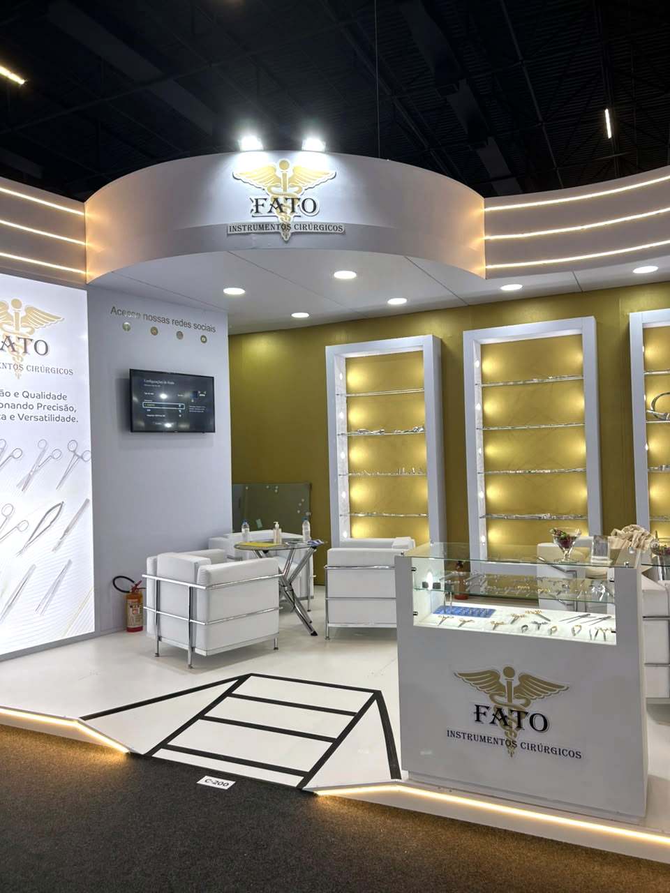 Estande da FATO em feira do setor hospitalar, com vitrines iluminadas e paredes douradas.