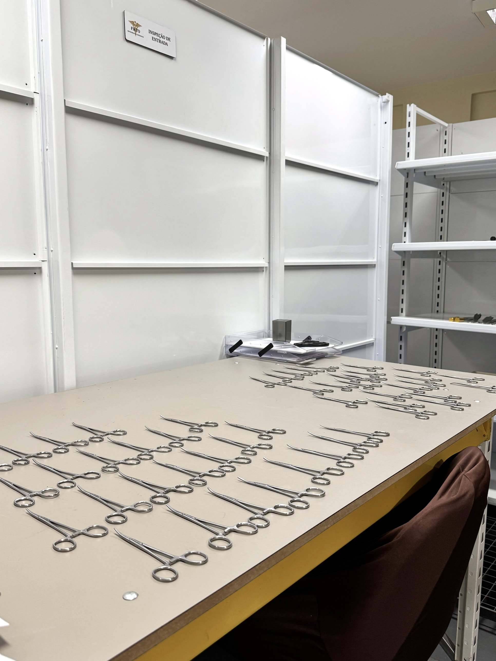 Bancada da sala de Inspeção de Entrada com pinças hemostáticas dispostas em fileiras para conferência.