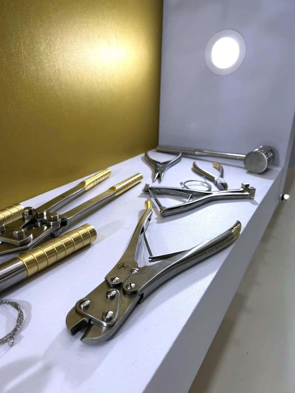 Instrumental ortopédico — alicates, cortadores e martelo — em exposição diante da parede dourada.
