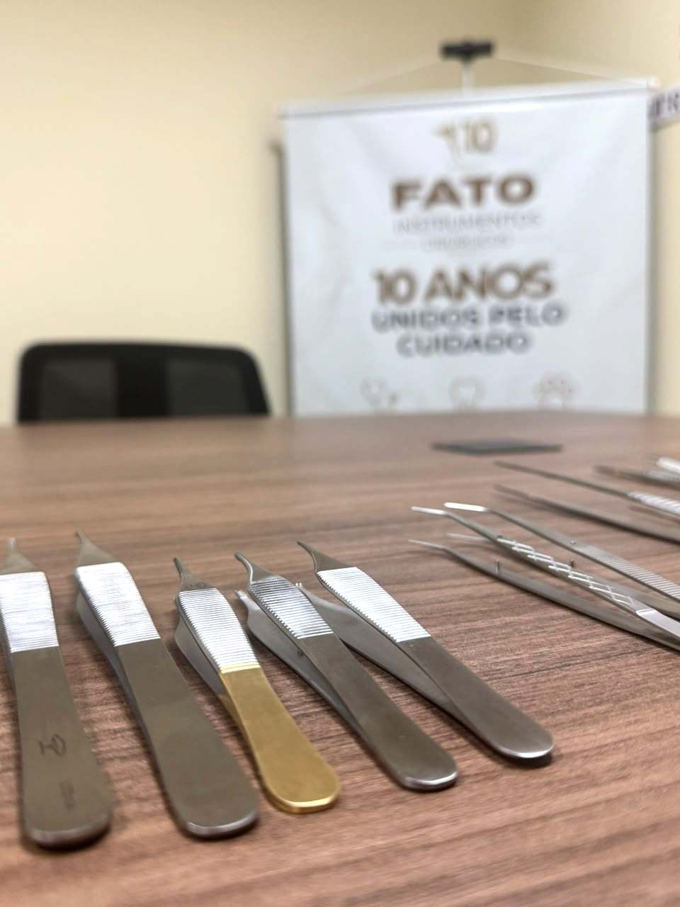 Pinças alinhadas sobre a mesa, com o banner "FATO 10 anos — Unidos pelo cuidado" ao fundo.
